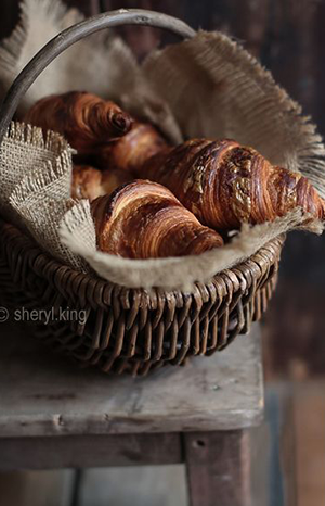 crooissants in a weave basket on top of a wood stool